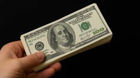 Рука тримає пачку доларів США на чорному фоні, крупним планом видно купюри по 100 доларів, бізнес до 10000 доларів